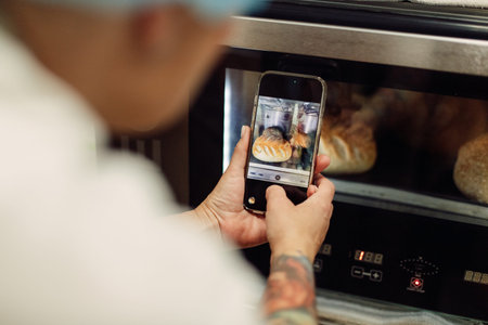 Cropped shot of a baker taking a picture on their cellphone of a selection of freshly baked bread.