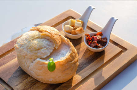 Homemade mushroom cream soup in bread bowl, served with bacon and biscuits.