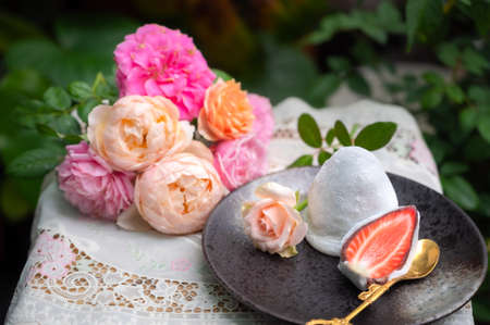 Daifuku stuffed with strawberries, a delicious Japanese dessert on a table with colorful roses flower and a view of the rose garden.の写真素材