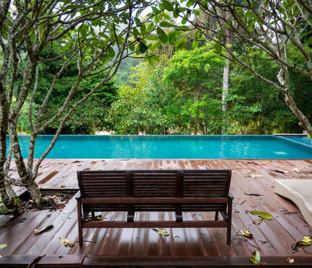 Wooden bench in home by the swimming pool with a warm tropical jungle rain falling in Thailand.の写真素材