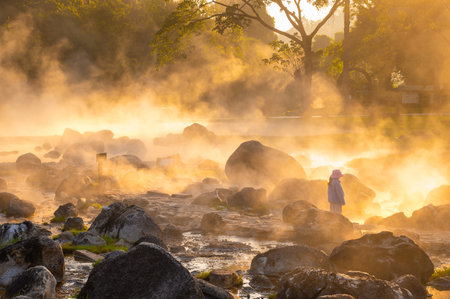 A little girl tourist looking at the steam of the natural hot springs reflects the beautiful morning sunlight at Chae Son National Park, Lampang, Thailand. Amazing Thailand.の写真素材