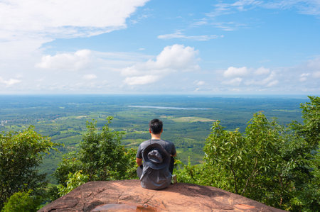 Stunning view of a man enjoying a beautiful green field  sitting on top of a mountain Naka Cave in Phu Lanka National, Thailand.の写真素材