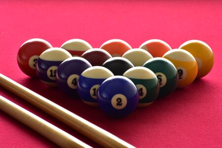 Numbered billiard balls with two pool cues on a red table.