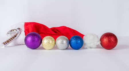 Santa Claus hat on a white background with balls of various colors and a silver cane.