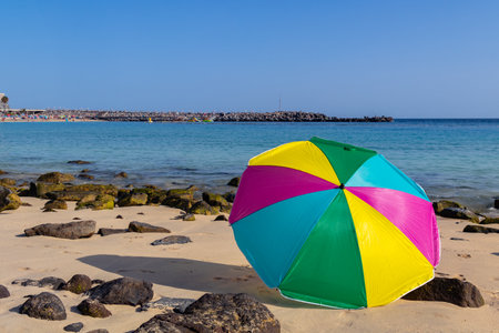Beach umbrella of various colors, placed on the sand of a yellow sand beach near the sea with rocks around with blue sea and skyの写真素材