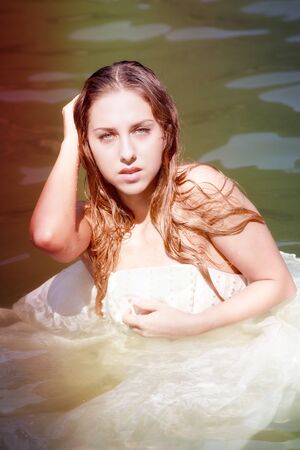 The Bride swimming in water in a white wedding dress, close-up. Vertical alignment.の写真素材