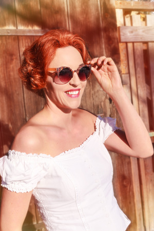 Young redhead woman with shoulder-free blouse and sunglasses enjoys the sun in the spring.の写真素材