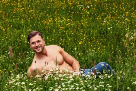 Muscular young man reading a naked torso in a flower meadowの写真素材
