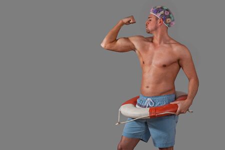 Young man shows off his muscles, with shower hood and life ring against grey backgroundの写真素材