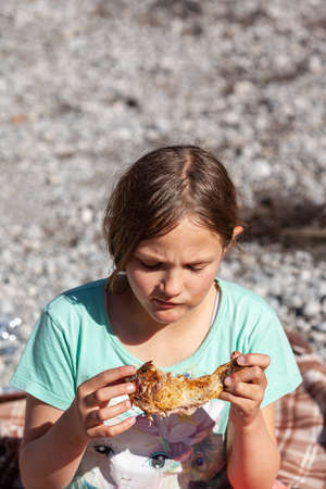 Young girl with a chicken leg in her hand at a picnic.の写真素材