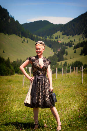 Blonde woman in black designer lace dirndl with open neckline and bag with matching hairstyleの写真素材