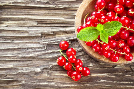 Red currant in a wooden plate on a wooden background. Top view with copy space.