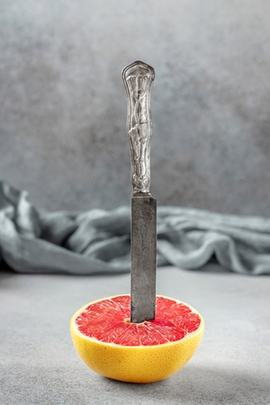 Ripe half of pink grapefruit citrus fruit on the stone table. Slice of grapefruit with knifeの写真素材