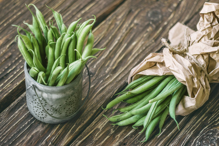 Pods of fresh green beans in paper bag and in a bowl on a rustic table 