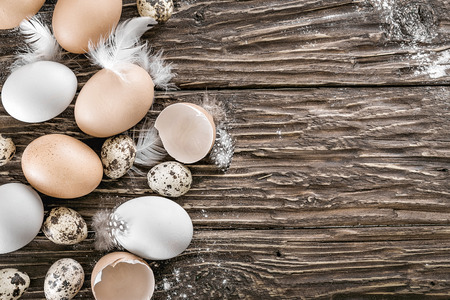 Chicken and quail eggs with feathers on a wooden table. Space for a text, view from aboveの写真素材