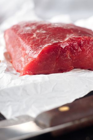 Large piece of uncooked beef lying on the white paper and a knifeの写真素材