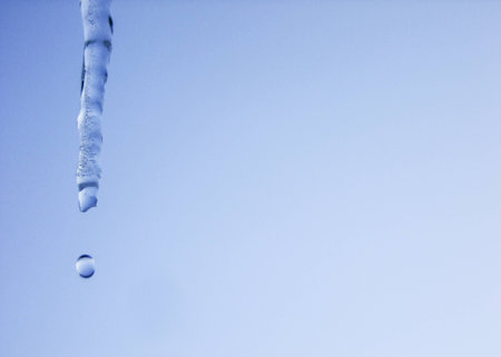 Icicle and falling Water Drop from it in blue Sky Background