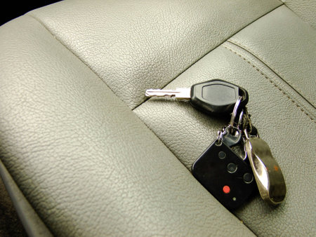Car Keys with Alarm Remote and Pendant on the Background of Front Leather Seat of A luxury Car