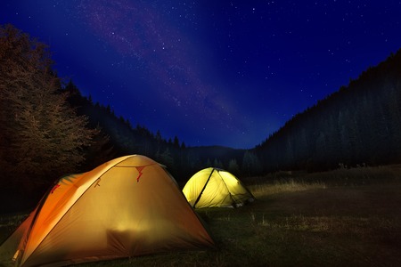 Photo of camp with glowing tents in front of milkyway night sky in the mountainsの写真素材