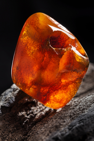 Natural amber. A piece of yellow and red semi transparent natural amber on piece of stoned wood.の写真素材