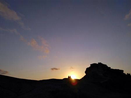 Couple - man and woman silhouette at the top of the mountain in front of sunset. Hiker rest on the rock. Background with copyspace. Symbol of romance, motivation, success, achievementの写真素材