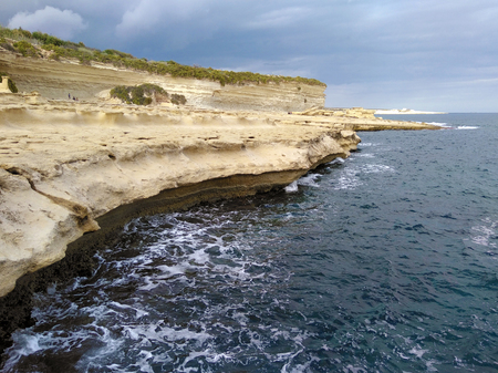 St peters pool. Malta coactline with cliff and rock with dark blue navy sea ocean and waveの写真素材