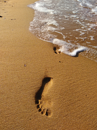 Lonely footprint at the beach. Trace at sand and sea wave. Peaceful lonely mood. Psychology or phylosophy symbol.の写真素材
