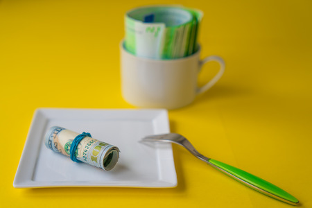 Roll of dollar hundred banknote on a white plate with a forkの写真素材