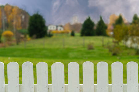 Nature autumn background with white wooden fence and green grass, blurred fall landscape.