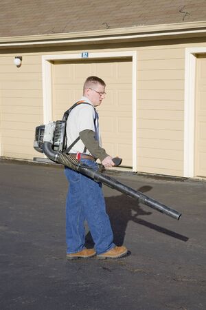 Worker using gas powered blower to clean leaves of the parking lot