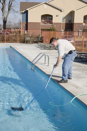 Service man cleaning pool filters, removing leaves that have fallen in pool this fall