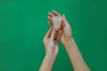 Menstrual cup on in hands on green background. Alternative feminine hygiene product during the periodの写真素材