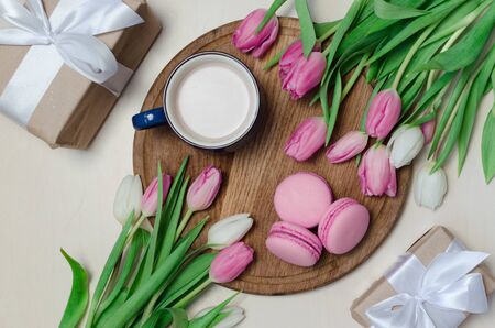 Coffee cup, spring tulip flowers and pink macarons on pastel table top view. Greeting for Womans or...