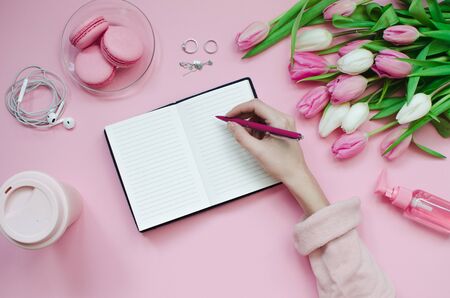 Girl writing wish list of future plans. flat lay composition with flowers, notepad, a cup of coffee and sweetsの写真素材