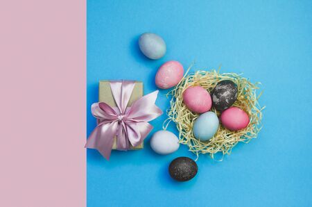 Easter eggs and nestle with colorful eggs with gift on pink and blue background