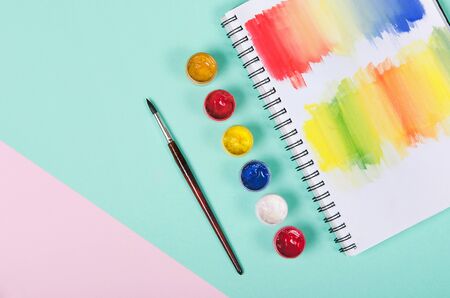 Bottles with paint and brush with colored notepad on white