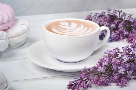Lilac, coffee cup with latte art and white and pink marshmallow on white wooden table. Romantic morning. Flat layの写真素材