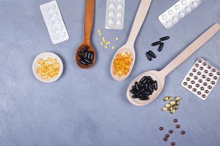 Black and yellow pills on wooden spoons or packed on gray backgroundの写真素材