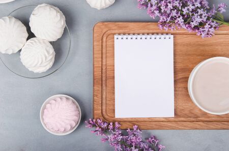 Lilac, coffee cup with latte art and notepad and marshmallow on white wooden table. Flat layの写真素材