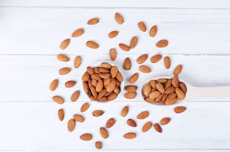 Flatlay view of almond seeds and wooden spoon on white wooden table plateの写真素材
