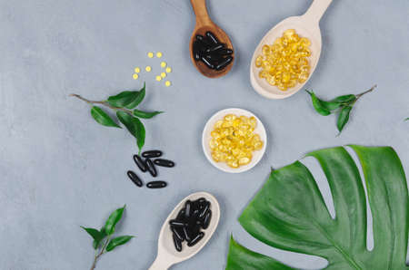 Black and yellow pills on wooden spoons on gray background. Flatlayの写真素材