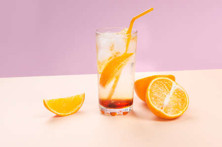 Orange alcohol cocktail with orange fruit slice on pink and yellow backgroundの写真素材