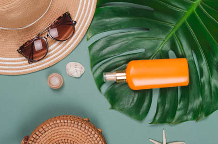 Summer straw hat, tropical monstera leaf, sunglasses, shells, suncream, starfish on green...