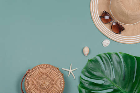 Summer straw hat, tropical monstera leaf, sunglasses, shells, starfish on green background. top...