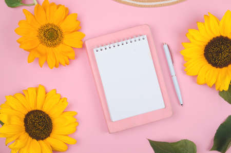 Creative flat lay of workspace desk, notepad and sunflower on pink backgroundの写真素材
