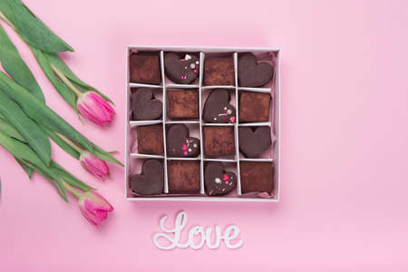 Present box with chocolate sweets hearts and tulips on pink background. Desert for Valentine Day