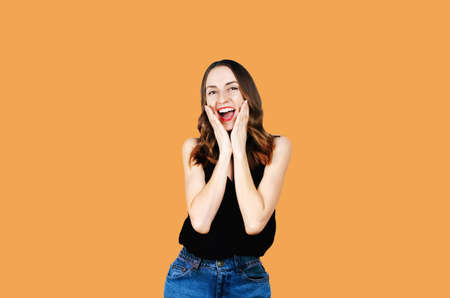 Surprised happy young woman with red lips looking sideways. Isolated on orange background
