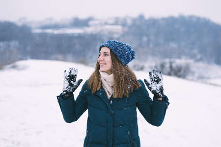 Young pretty woman in winter clothes and gloves with snow smiling.