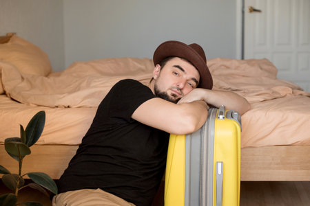 Young man sitting bored on n suitcase waiting for summer vacation during  season. Lockdown conceptの写真素材