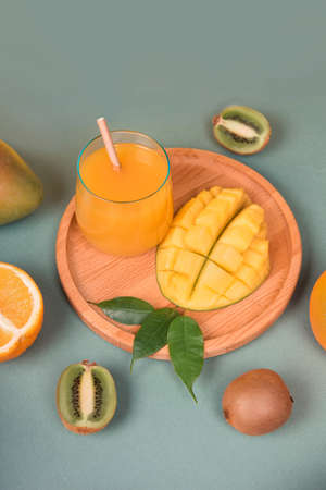 Glass of fresh orange and mango juice, kiwi, on green background